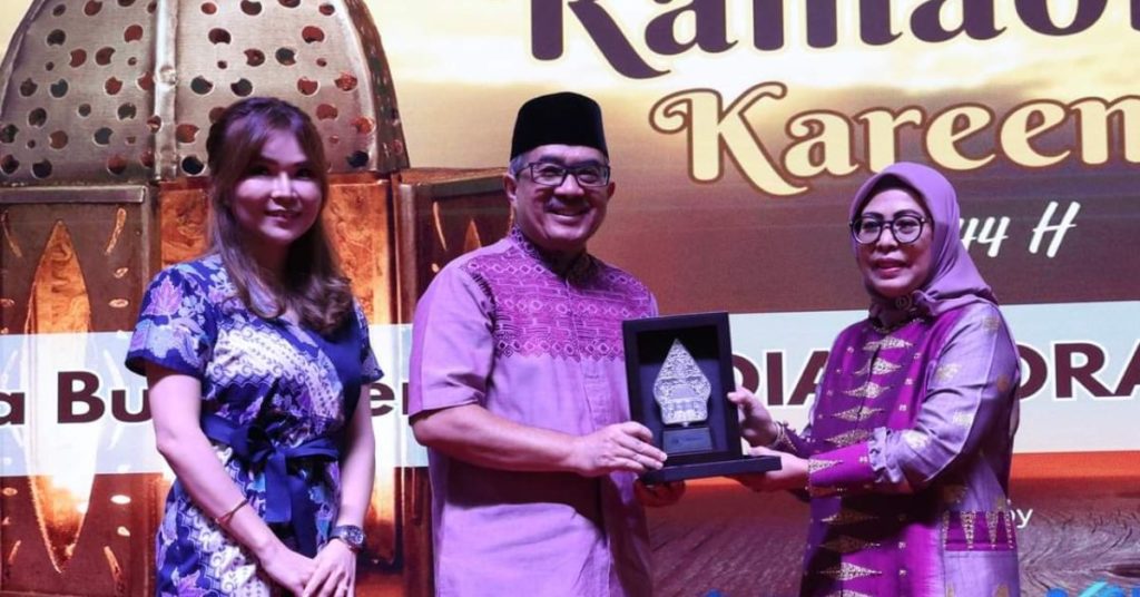 three people sanding, woman on the left giving the man in the middle a plaque, the woman on the right is smiling to the camera